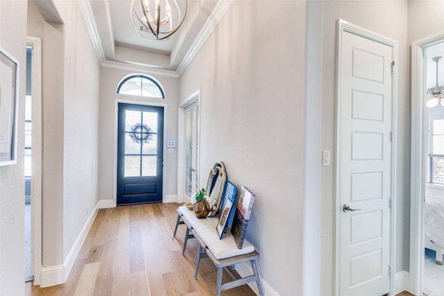 foyer entrance with crown molding, baseboards, light wood-type flooring, a notable chandelier, and a raised ceiling