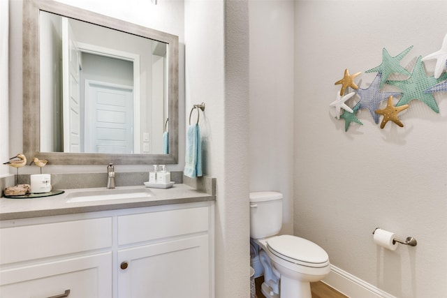 half bath featuring toilet, baseboards, and vanity