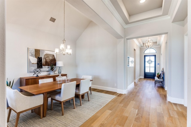 dining area with a tray ceiling, light wood-type flooring, a notable chandelier, and visible vents