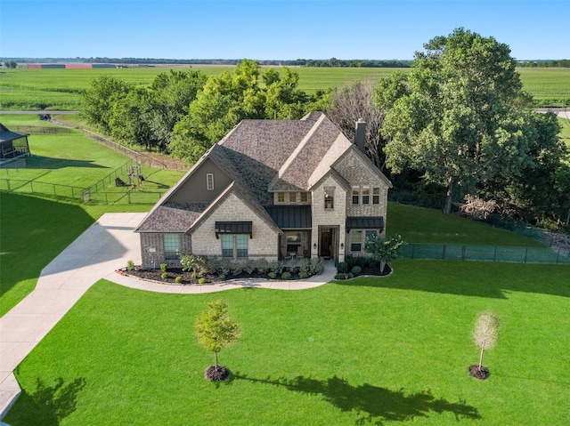 view of front of house featuring a front yard, fence, a shingled roof, a chimney, and a rural view