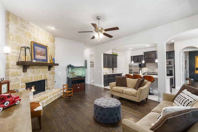 living area with a ceiling fan, wood finished floors, arched walkways, a fireplace, and baseboards