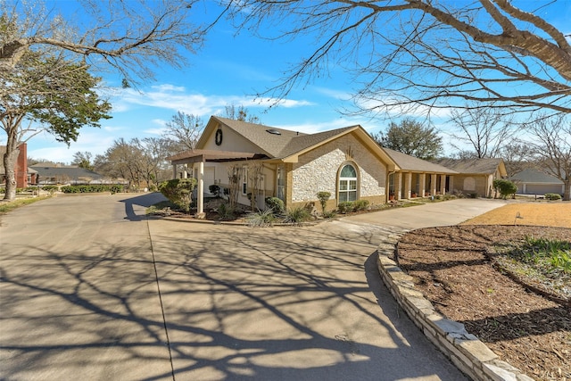 view of front facade with stone siding, driveway, and a shingled roof