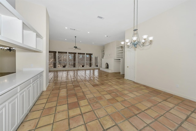 interior space featuring visible vents, a fireplace with raised hearth, light countertops, white cabinetry, and ceiling fan with notable chandelier