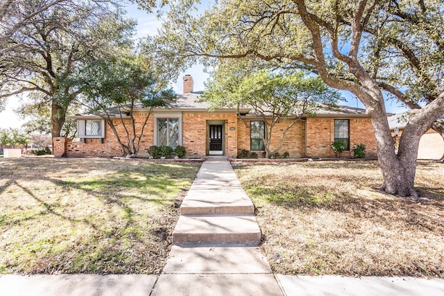 ranch-style home featuring brick siding, a chimney, and a front yard