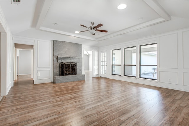 unfurnished living room featuring a raised ceiling, a decorative wall, a brick fireplace, and light wood-type flooring