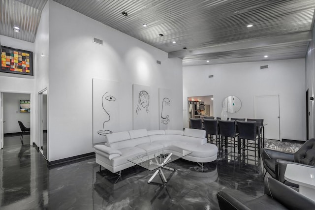 living area with visible vents, concrete floors, a high ceiling, and baseboards