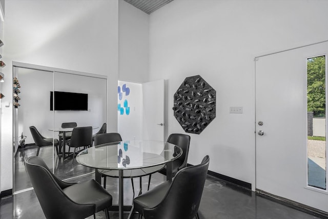 dining space with baseboards, concrete floors, and a towering ceiling