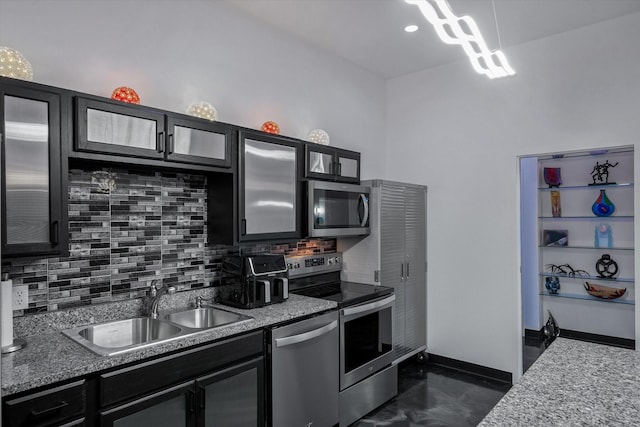 kitchen featuring decorative backsplash, a sink, stainless steel appliances, glass insert cabinets, and dark cabinets