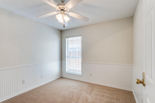 spare room with a ceiling fan, carpet floors, a textured ceiling, and wainscoting