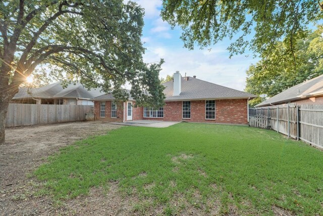 rear view of property with a fenced backyard, a yard, an outdoor structure, brick siding, and a chimney