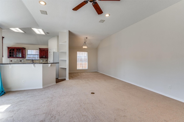 unfurnished living room with light colored carpet, vaulted ceiling, a ceiling fan, and baseboards