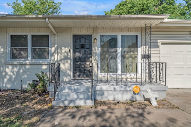 view of exterior entry featuring crawl space, a garage, brick siding, and covered porch