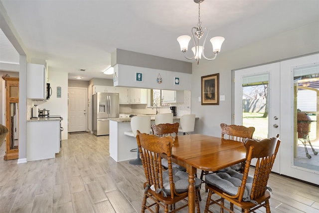 dining area with french doors, a notable chandelier, and light wood-style flooring