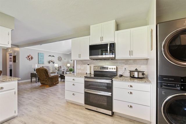 kitchen featuring decorative backsplash, stacked washer and dryer, appliances with stainless steel finishes, and white cabinetry