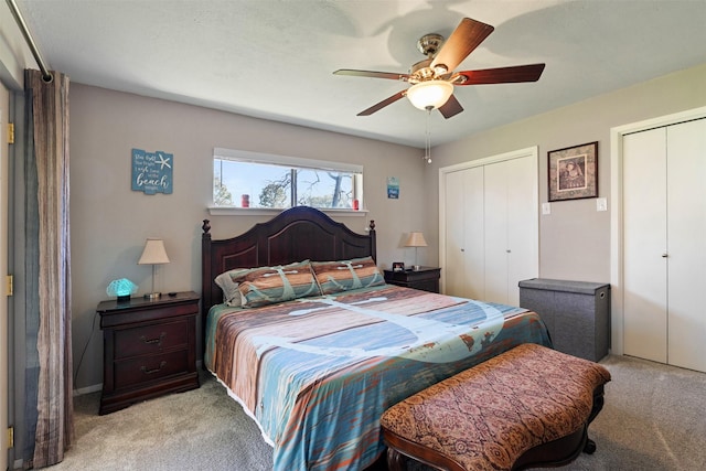 bedroom featuring light carpet, ceiling fan, and multiple closets