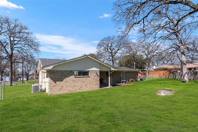 back of property with a lawn, fence, cooling unit, a fire pit, and brick siding