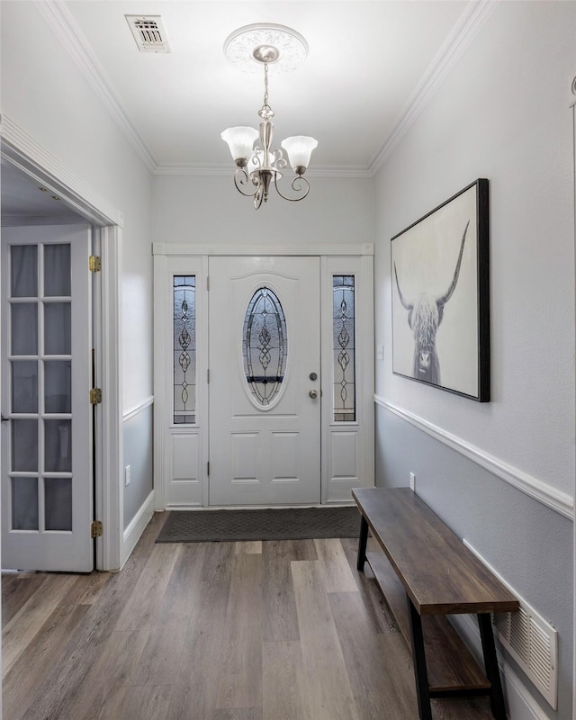 entryway featuring visible vents, a notable chandelier, wood finished floors, and crown molding