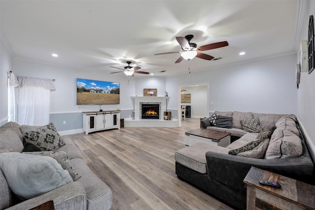 living room featuring ornamental molding, a warm lit fireplace, recessed lighting, light wood-style floors, and baseboards