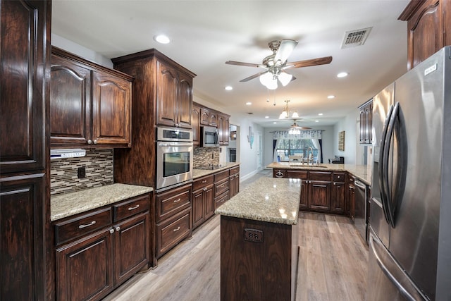 kitchen with stainless steel appliances, a peninsula, a center island, and light wood finished floors