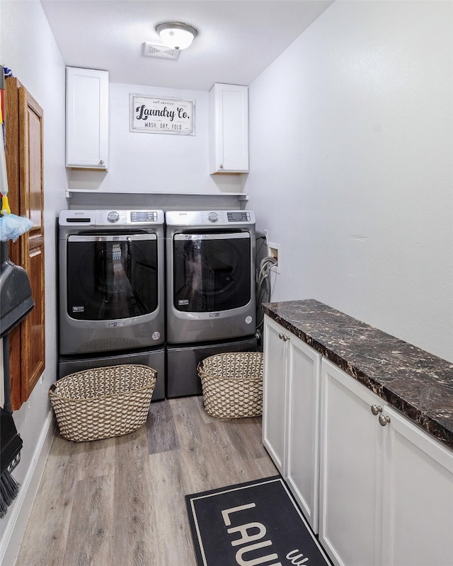 clothes washing area with washer and dryer, wood finished floors, and cabinet space