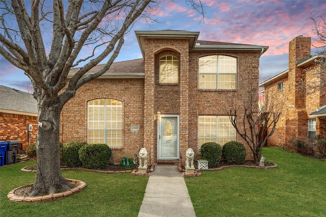 traditional-style house featuring brick siding, a shingled roof, and a front yard