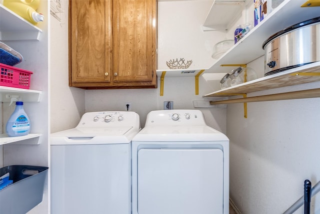 clothes washing area with separate washer and dryer and cabinet space