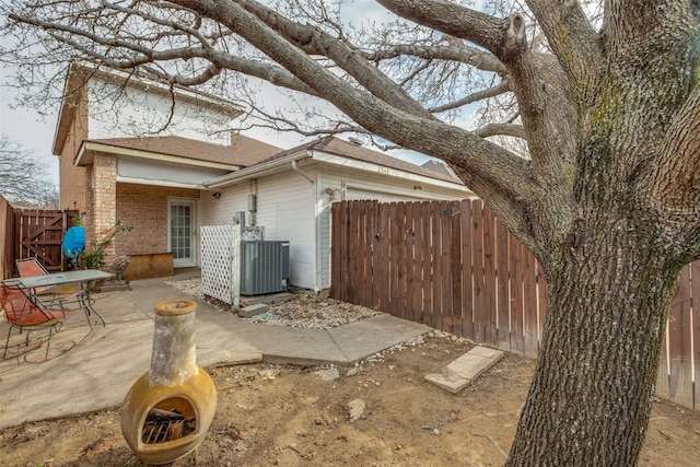 view of side of property featuring a patio, fence, cooling unit, an attached garage, and brick siding