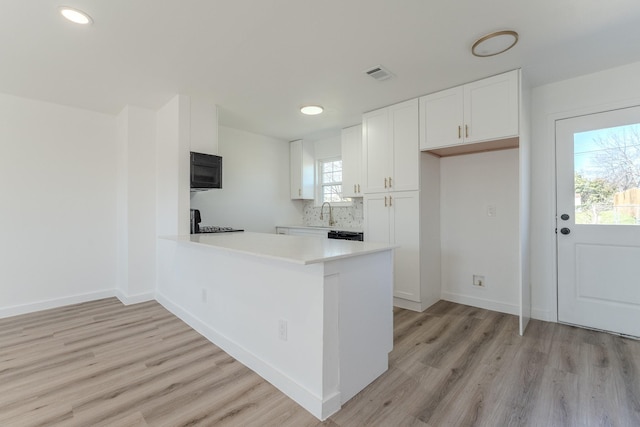 kitchen with white cabinets, light wood-style flooring, visible vents, and black microwave