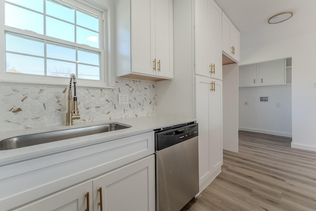 kitchen with light wood finished floors, backsplash, stainless steel dishwasher, white cabinets, and a sink