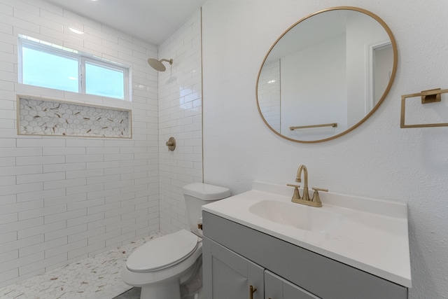 full bathroom featuring vanity, toilet, a textured wall, and a tile shower