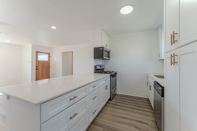 kitchen with light stone countertops, light wood-type flooring, a peninsula, white cabinets, and stainless steel appliances