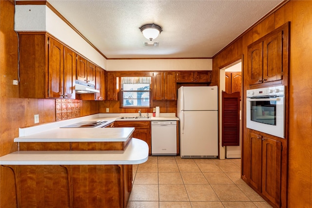 kitchen featuring visible vents, under cabinet range hood, a sink, white appliances, and a peninsula