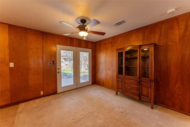 entryway featuring light carpet, visible vents, wood walls, and a ceiling fan