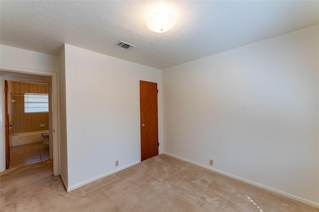 unfurnished bedroom featuring visible vents, light carpet, a textured ceiling, and baseboards