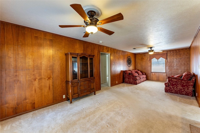 unfurnished room with a ceiling fan, wooden walls, light colored carpet, and a textured ceiling