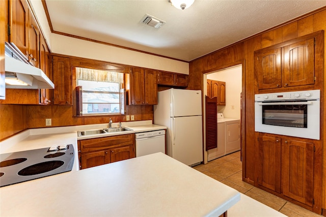 kitchen with white appliances, visible vents, washing machine and clothes dryer, a sink, and under cabinet range hood