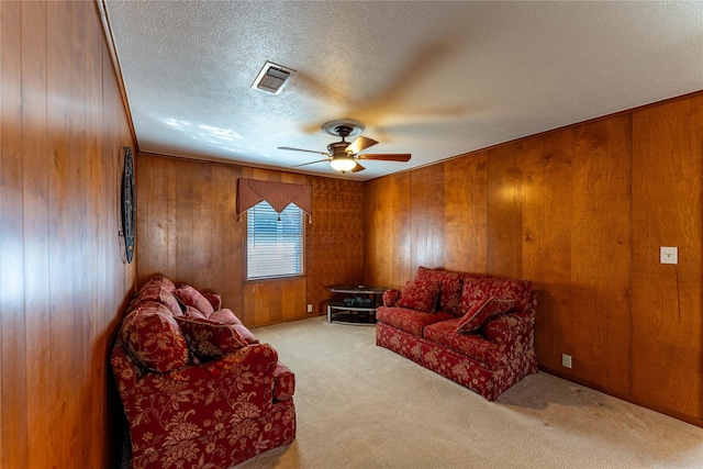 living area with carpet, visible vents, ceiling fan, wood walls, and a textured ceiling