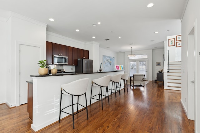 kitchen featuring a kitchen bar, dark countertops, appliances with stainless steel finishes, and dark wood-style flooring