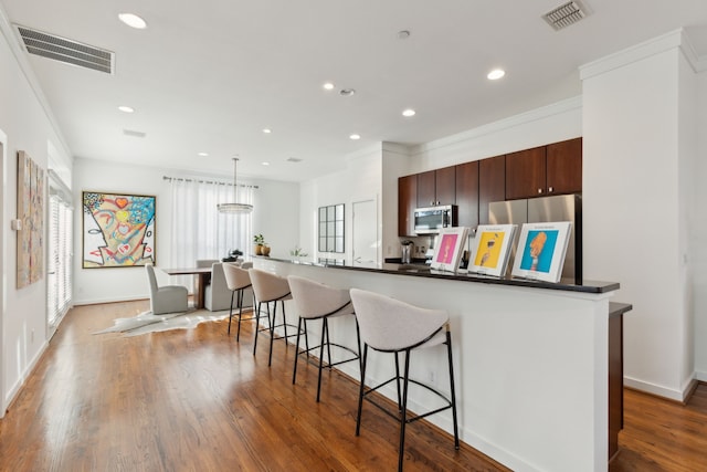 kitchen featuring visible vents, a kitchen breakfast bar, appliances with stainless steel finishes, and wood finished floors