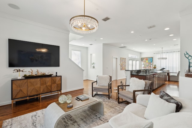 living room featuring recessed lighting, crown molding, an inviting chandelier, and wood finished floors