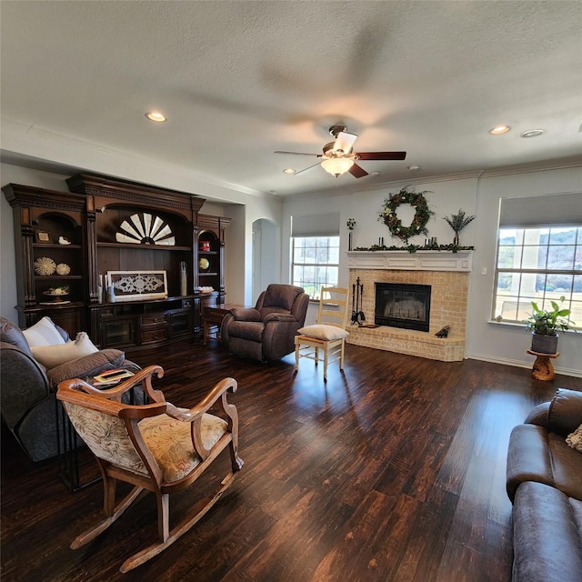 living room with a brick fireplace, ornamental molding, wood finished floors, arched walkways, and a textured ceiling