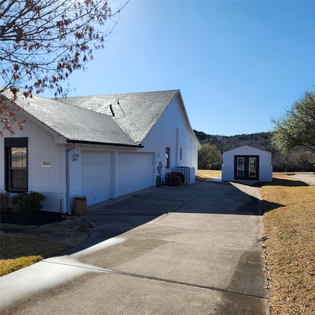 view of side of home with french doors, an attached garage, driveway, and a shingled roof