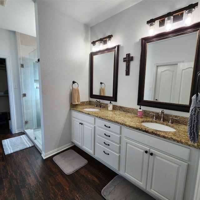 bathroom featuring double vanity, a shower stall, wood finished floors, and a sink