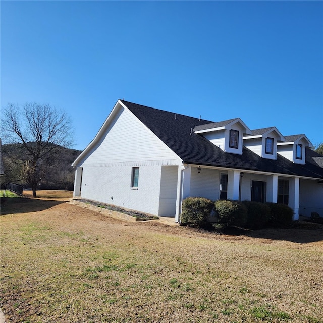 view of side of property featuring a lawn, brick siding, and a shingled roof