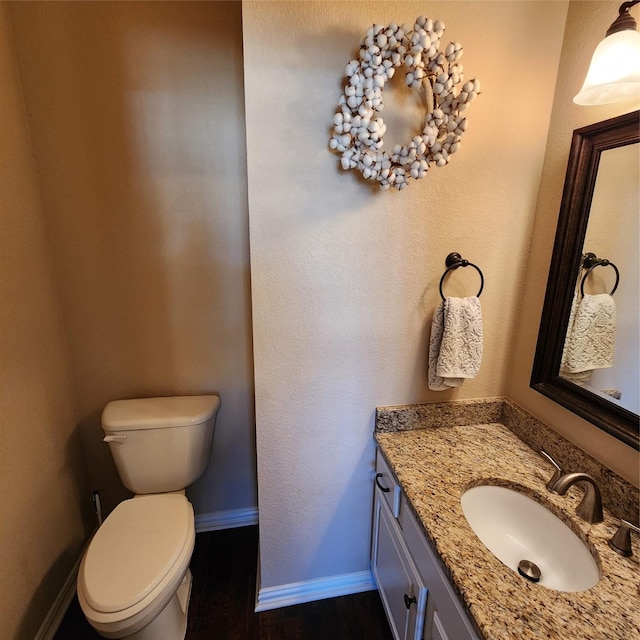 half bathroom featuring baseboards, toilet, wood finished floors, and vanity