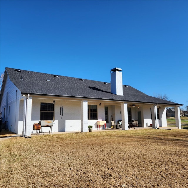 back of property featuring a patio area, a lawn, roof with shingles, and a chimney