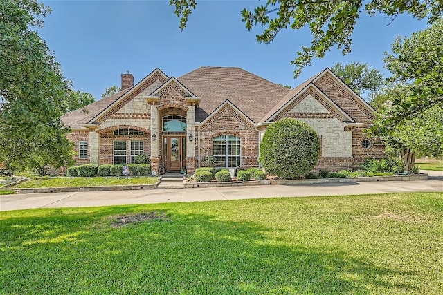 french provincial home with a front yard, brick siding, stone siding, and a chimney