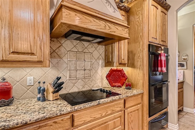 kitchen with premium range hood, light stone counters, decorative backsplash, black appliances, and a warming drawer