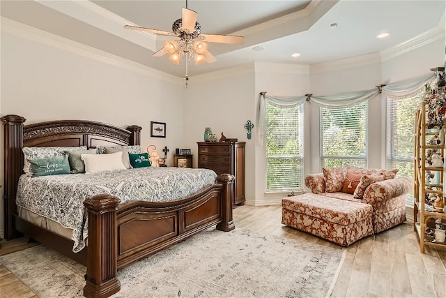 bedroom featuring a raised ceiling, light wood-style floors, ceiling fan, and crown molding