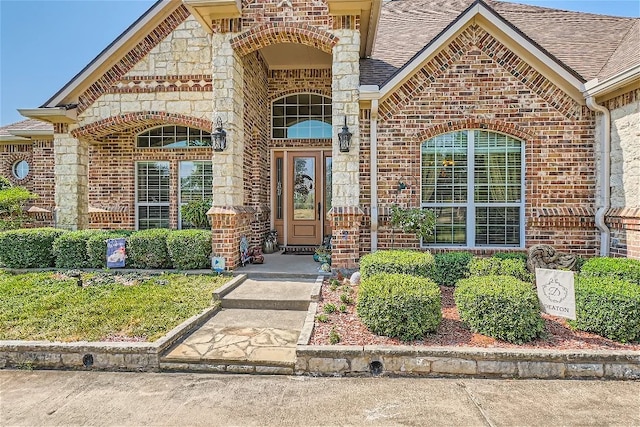 doorway to property with stone siding, brick siding, and roof with shingles